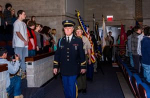 Military personnel in ceremonial procession indoors.