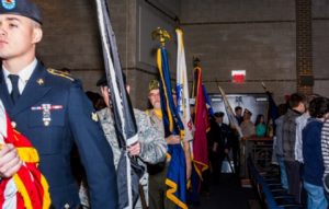 Military personnel carrying flags at ceremony.