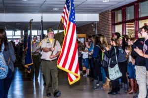 Color guard procession in school hallway with clapping students.