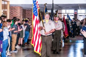 Veterans carrying flags in school ceremony.