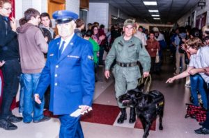 Veterans walking with service dog in crowded hallway.