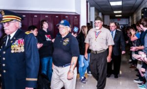 Veterans walking hall of honor with applauding students.