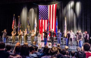 Veterans' ceremony with US flag on stage before audience.