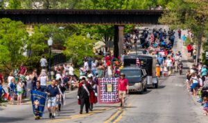 Crowded street parade with onlookers and a marching band.