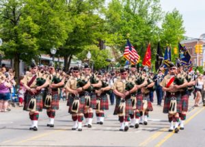 Bagpipe band marching in parade with crowd.