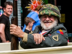 Smiling man in military costume holding rifle at event.