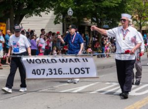 Veterans marching with WWII remembrance banner in parade.