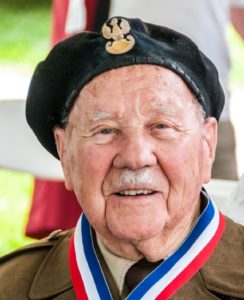 Elderly veteran smiles wearing beret and medals.