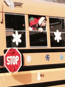 Child in elf hat looking out decorated school bus window.