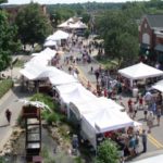 Outdoor street fair with white tents and crowds.
