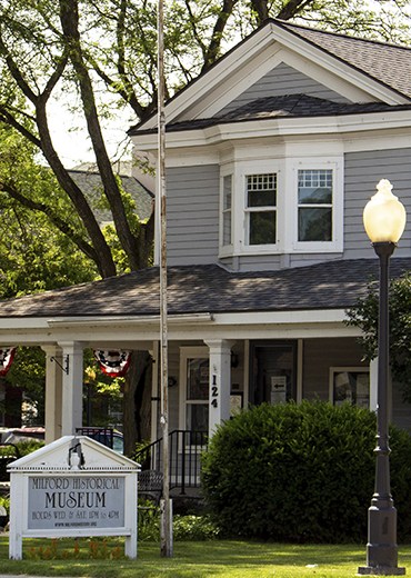 Historic house-style Milford Historical Museum facade with sign and lamp.