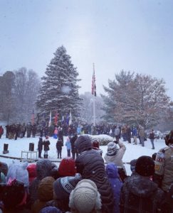 People at snowy outdoor ceremony with American flag.